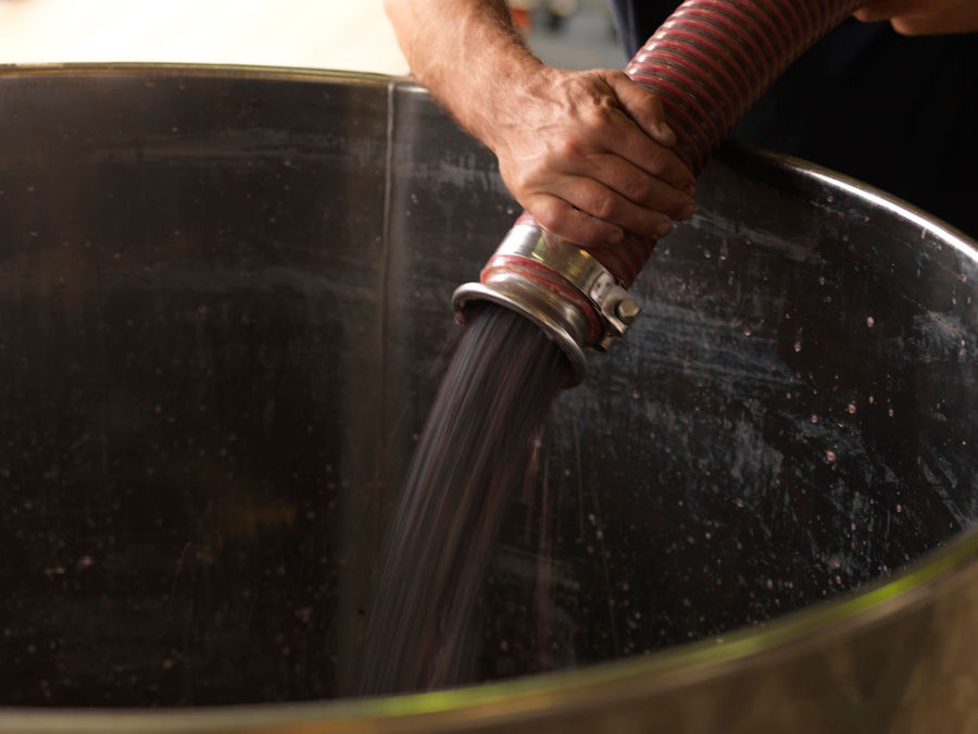 man holding a hydraulic pump and filling a vate at 'Strofilia winery plant